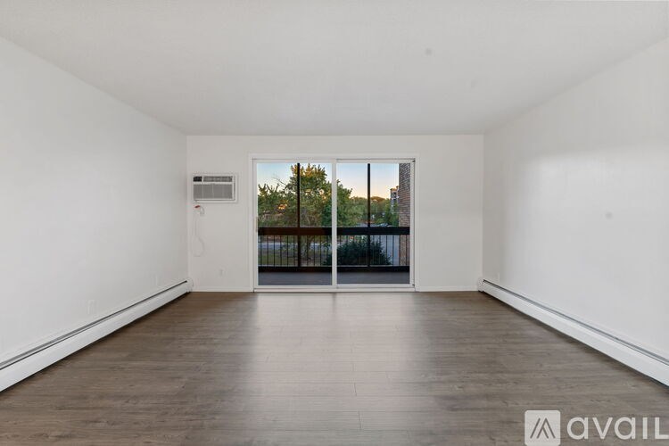 A spacious room with wooden flooring and a view of trees through a glass door.