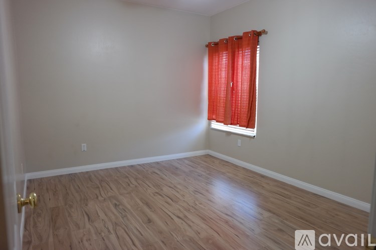 A room with a wooden floor and a window with red curtains.