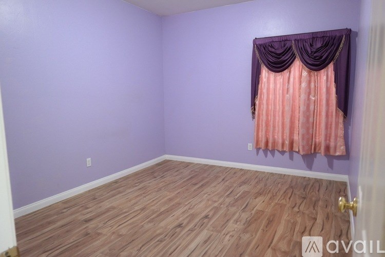 A room with purple walls and wooden flooring with a window covered by a pink curtain.