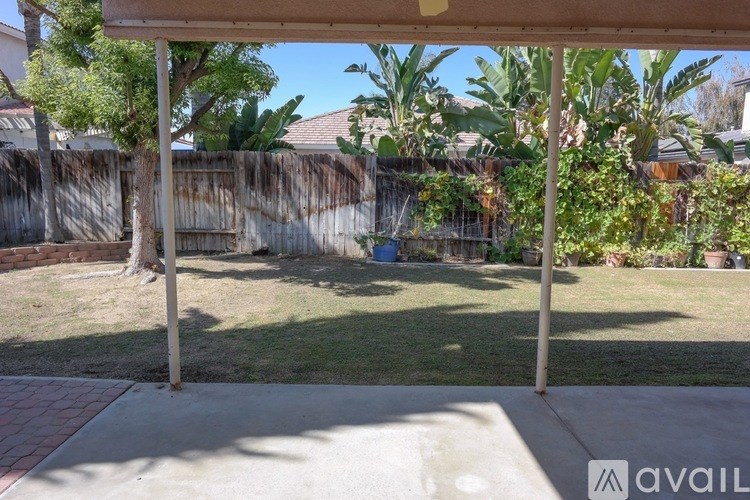 A patio with a table and chairs is covered by a roof and surrounded by a fence and plants.