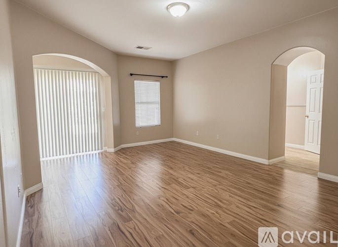 A spacious room with wooden flooring and arched doorways.