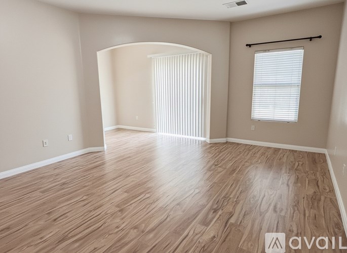 A spacious room with wooden flooring and a large arched window.