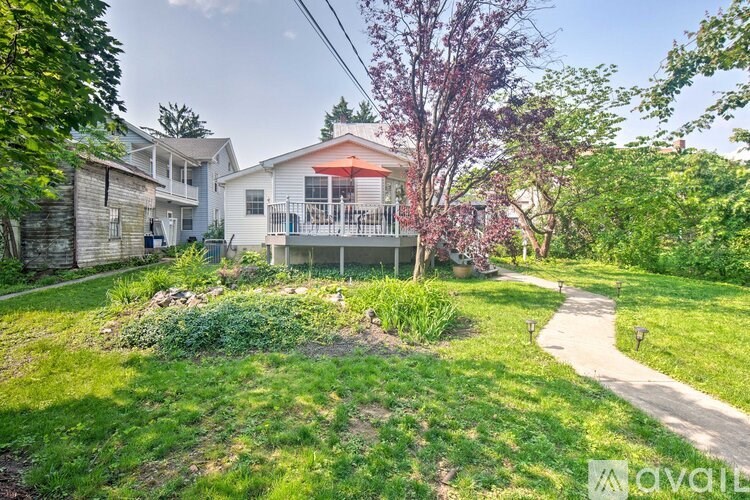 A house with a red awning is surrounded by greenery and a dirt path.