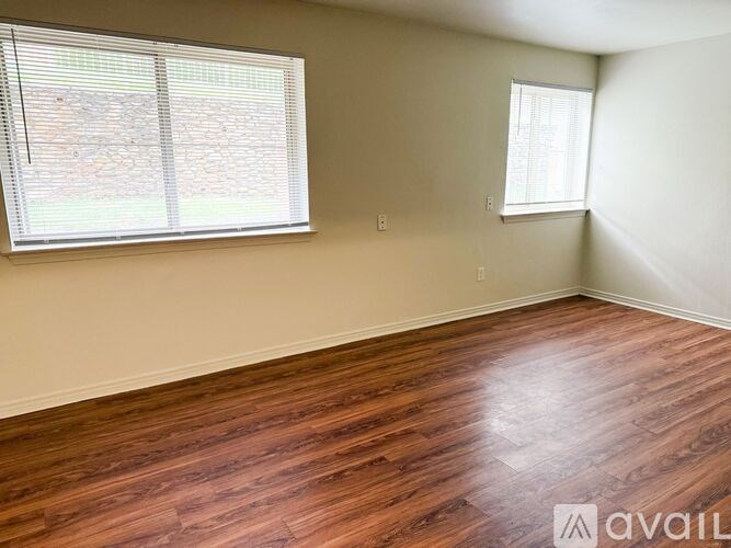 A room with wooden flooring and two windows.
