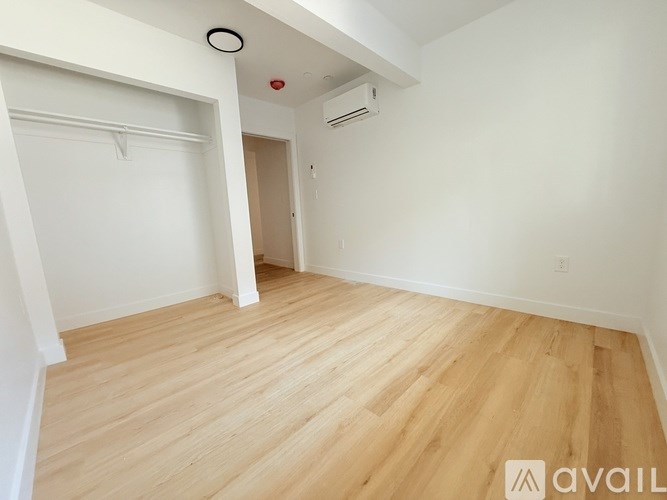 A room with wooden flooring and white walls, with a doorway leading to another room.