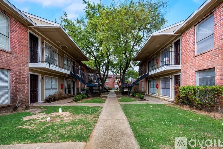 A red brick apartment building with a tree in front and a sidewalk.