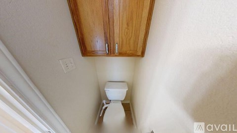 A white toilet is mounted under a wooden cabinet in a small room.