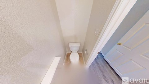 A white toilet in a narrow hallway with a door on the right.