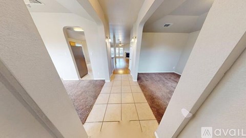 A hallway with a tiled floor and a carpeted area leading to a door.
