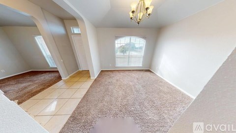 A spacious room with a rug, a chandelier, and a window overlooking a street.