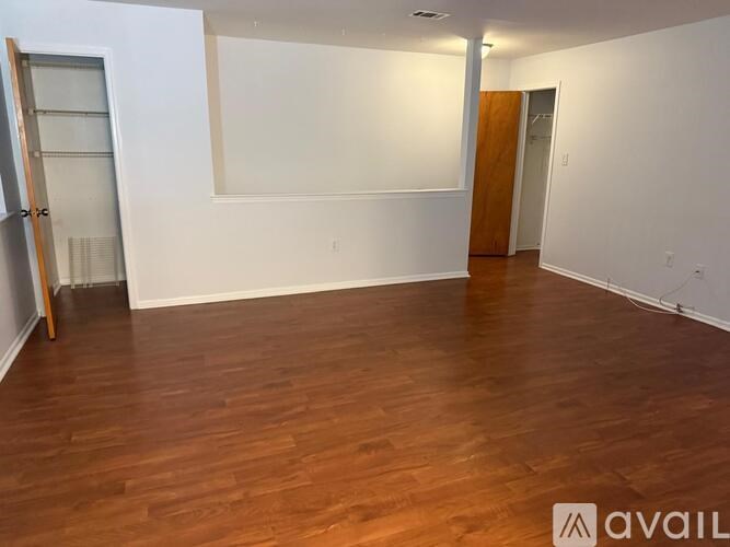 A room with wooden flooring and white walls, with a door on the right side.