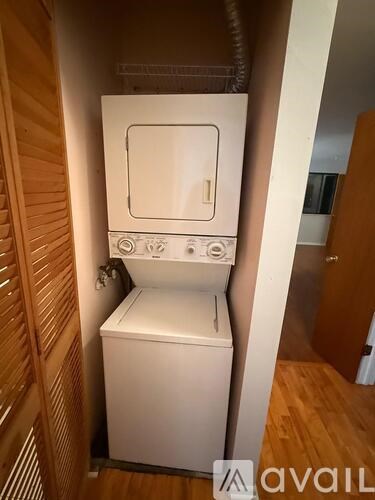 A small white washing machine sits in a narrow space between a wooden staircase and a wall.