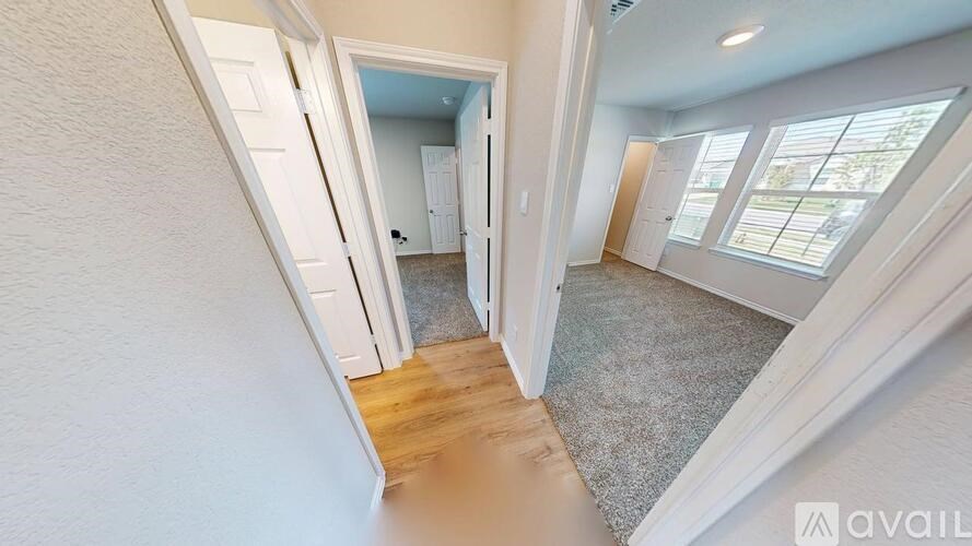 A hallway with a carpeted floor and white walls leading to a bedroom.