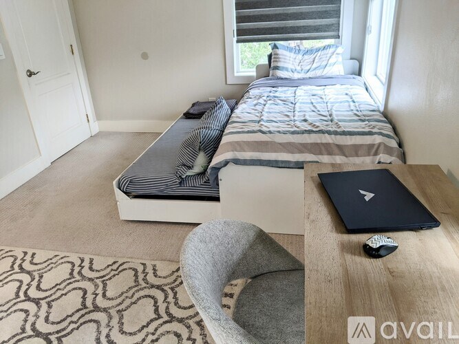 A bedroom with a bed, a chair, and a laptop on a table.