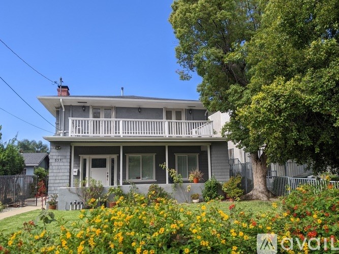 A house with a grey facade and a white porch surrounded by a garden with yellow flowers.