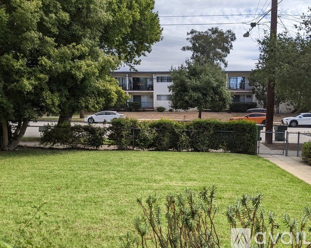 A grassy area with a tree and a fence in the foreground and a building in the background.