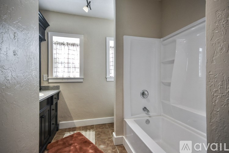 A bathroom with a white tub and a window with a white curtain.