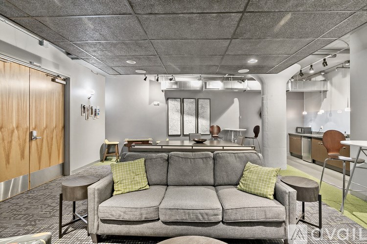 A grey couch with two green pillows sits in a room with a grey carpet.