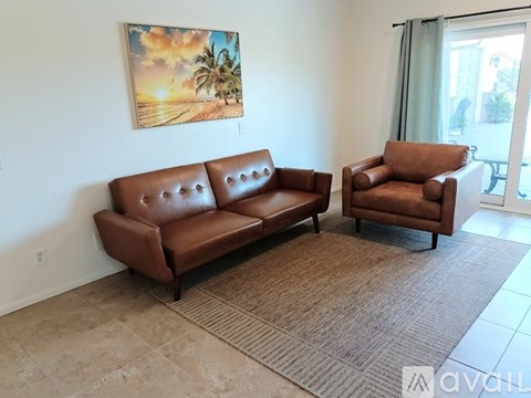 A living room with a brown leather couch and chair, a rug, and a painting of a beach scene on the wall.