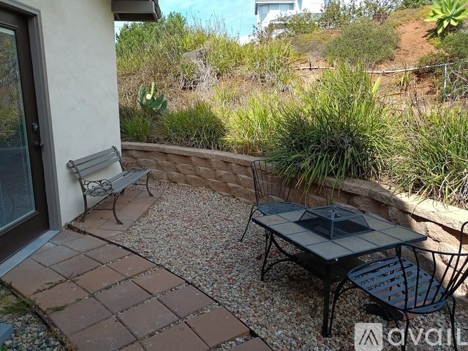 A patio with a table and chairs is surrounded by a gravel area and a wall.