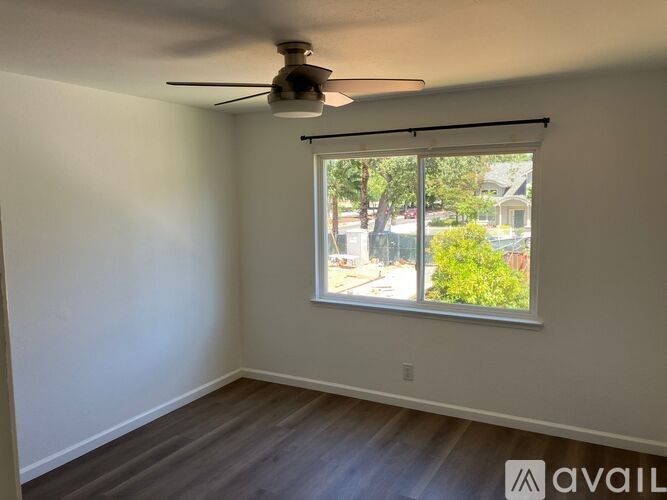 A room with a ceiling fan and a window overlooking a street.