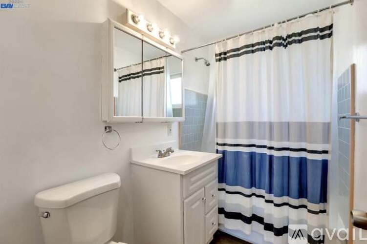 A white bathroom with a white toilet, sink, and a blue and white shower curtain.