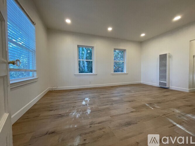 A spacious room with wooden flooring and two windows.