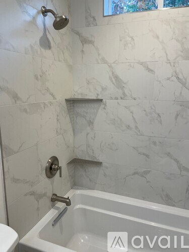 A white bathroom with a marble tile wall and a tub.