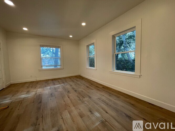 A room with wooden flooring and two windows.
