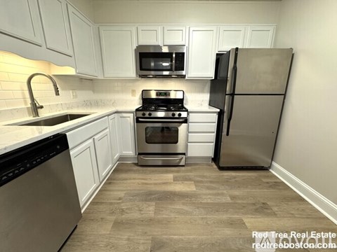 A kitchen with white cabinets and a black fridge.