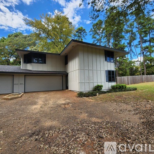A house with a garage is surrounded by trees and has a dirt driveway.
