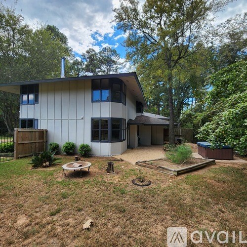 A house with a white exterior and a brown roof is surrounded by greenery.