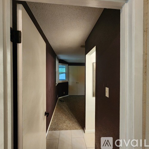 A hallway with a door on the left and a bathroom visible in the distance.