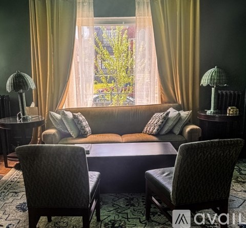 A living room with a couch, two chairs, and a table with a lamp on it.