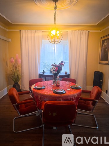 A dining room with a round table set for six with red chairs.