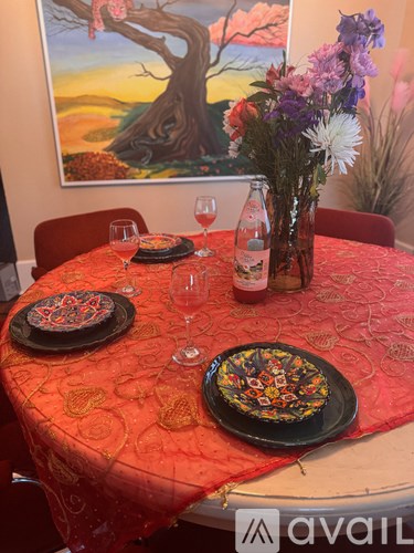 A table set for two with a red tablecloth and a painting on the wall.