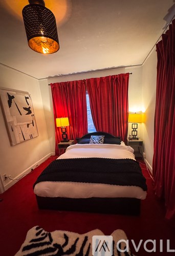 A bedroom with a bed, red curtains, and a hanging light fixture.