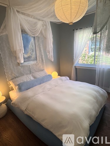 A bedroom with a canopy bed and a window with white curtains.