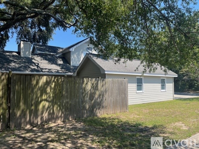 A house with a grey roof and a white wall with a window is surrounded by a wooden fence.