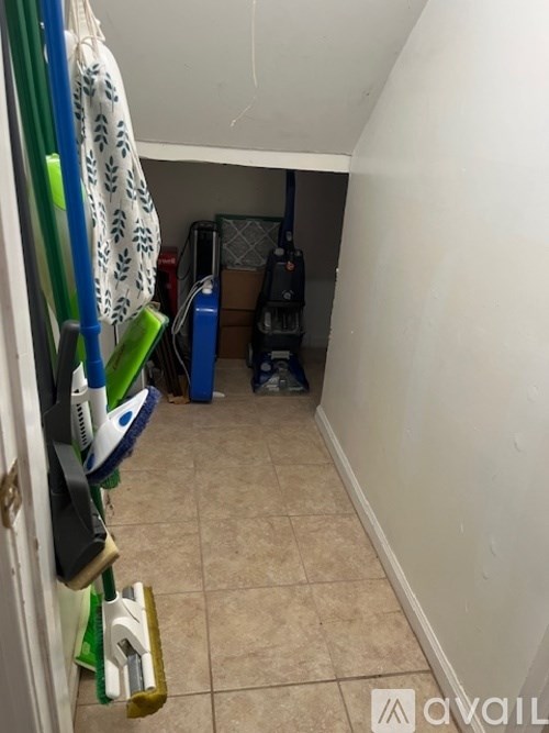 A small, untidy room with a white wall and a green broom.