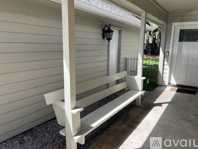 A white bench is on a porch with a black lantern on the wall.