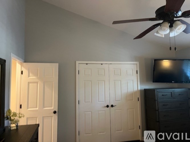 A room with a ceiling fan and a flat screen TV mounted on the wall.