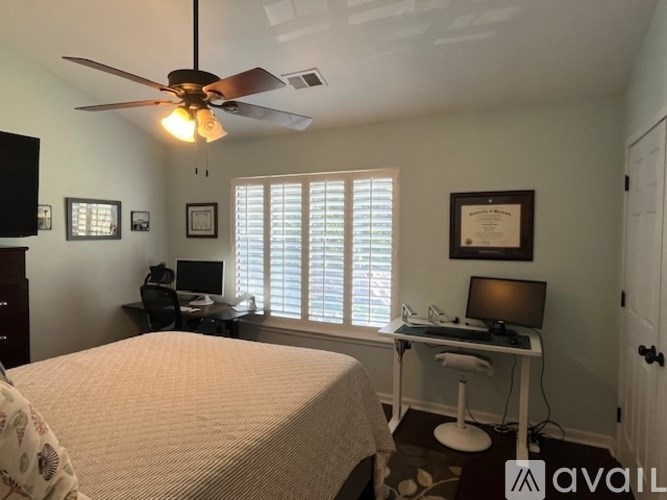 A bedroom with a bed, desk, and a ceiling fan.