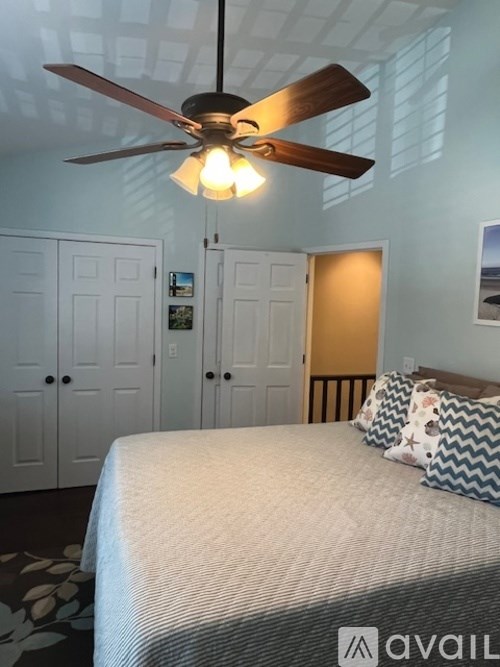 A bedroom with a bed, a ceiling fan, and a wall-mounted TV.
