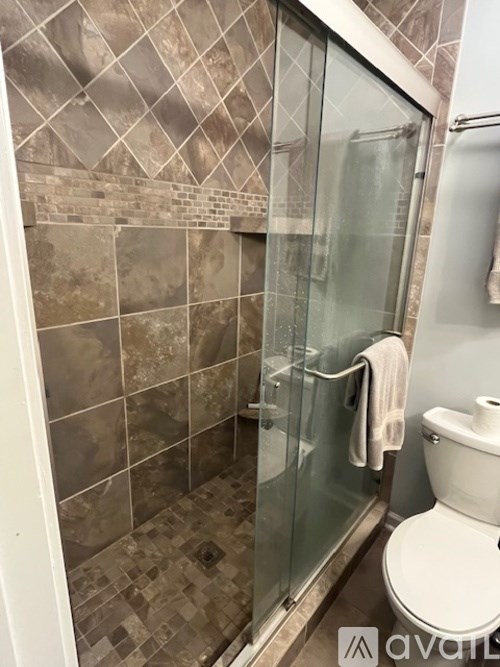 A bathroom with a toilet, a glass shower door, and a tiled wall.