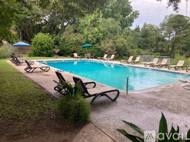 A pool surrounded by lawn chairs and trees.