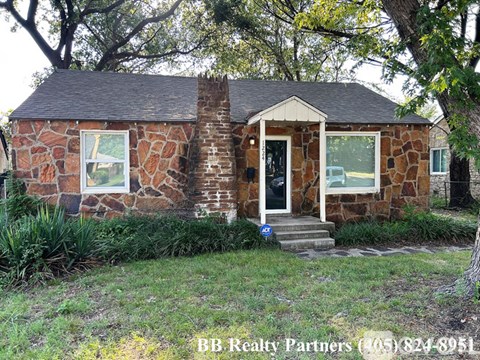 A small house with a stone facade is for sale, as indicated by the sign in front of it.