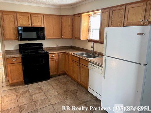 A kitchen with a black stove top oven, white refrigerator, and wooden cabinets.