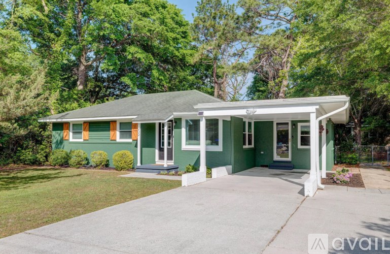 A green house with a porch and a white fence.