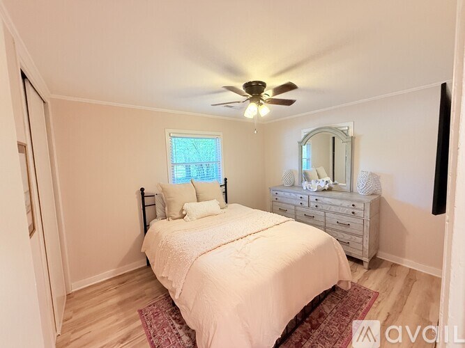 A bedroom with a bed, dresser, mirror, and window.